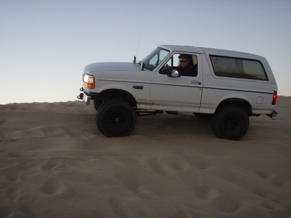 White Ford Bronco driving on sand dunes