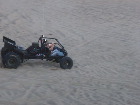 1994 Ford Bronco - A black dune buggy with two occupants is driving across a sandy terrain. The buggy has large off-road tires and a roll cage.
