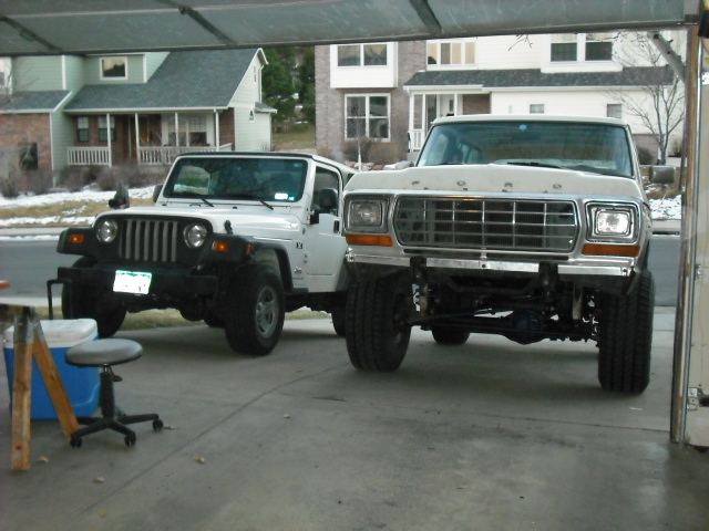 White Jeep Wrangler and 1979 Ford Bronco parked in a driveway.