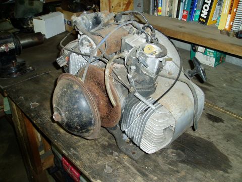 2000 Ford E350 - A rusty, air-cooled engine with a carburetor and a black bell-shaped cover is sitting on a wooden workbench. The engine appears to be from…