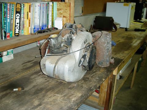 2000 Ford E350 - A workbench with an old engine, books, and a small white refrigerator. A spark plug is visible on the floor.