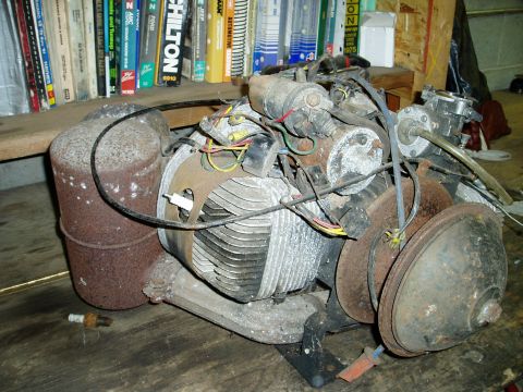 2000 Ford E350 - A rusty, vintage engine sits on a wooden surface, with a stack of automotive repair manuals visible in the background.
