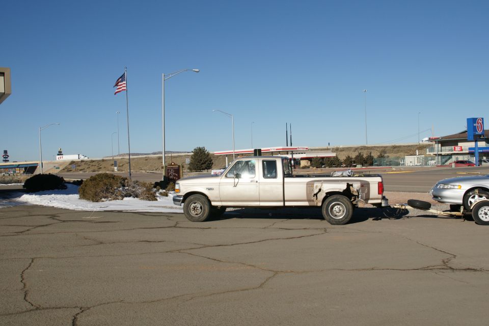 Tan pickup truck towing a silver sedan on a trailer.