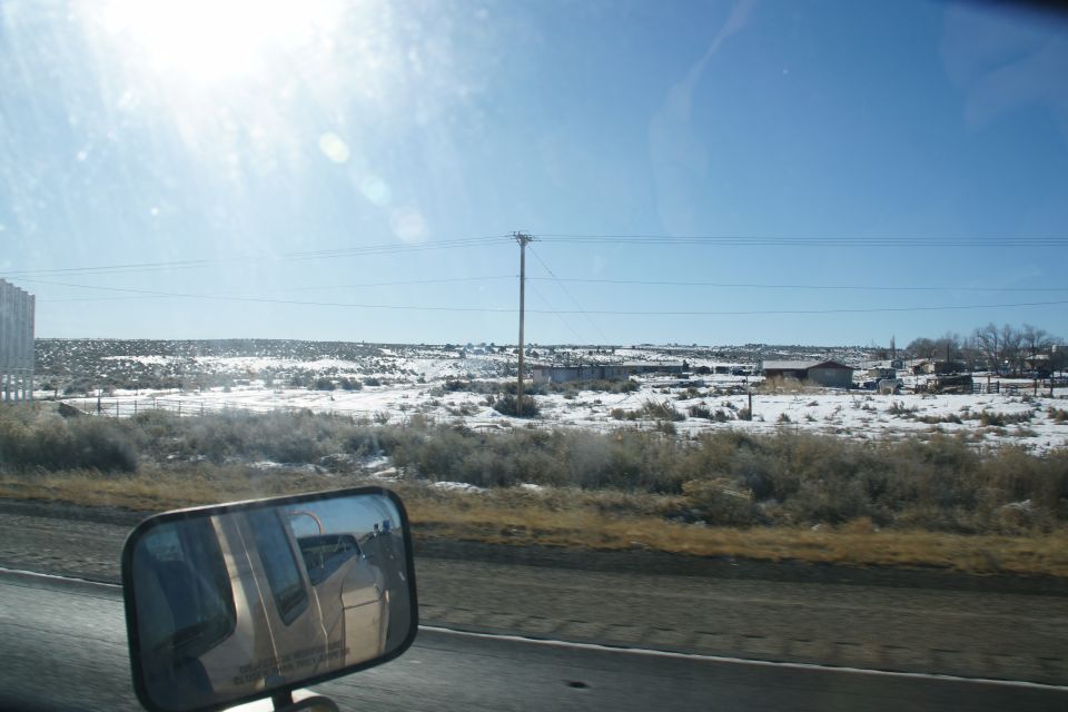 Side mirror reflection of a snow-covered rural landscape with buildings.