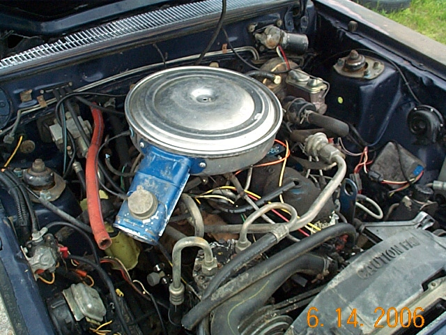 Engine bay of an older Ford with round air cleaner and blue valve cover