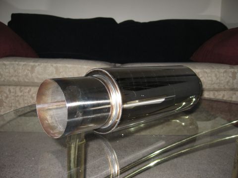 1991 Mitsubishi 3000GT - A shiny exhaust muffler is placed on a glass table, with furniture visible behind it.