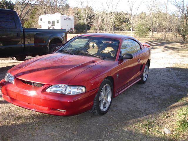 Red 1996 Ford Mustang coupe parked on dirt lot