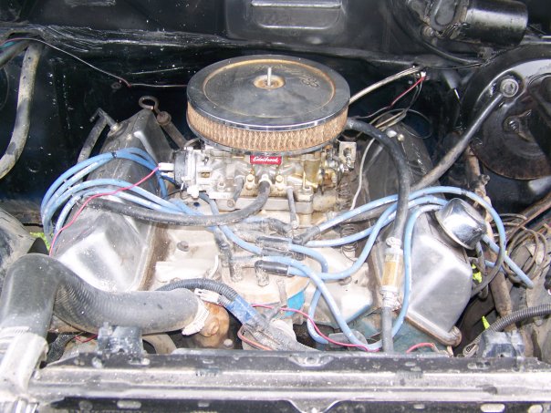Engine bay showing carburetor, air filter, spark plug wires, and radiator hoses