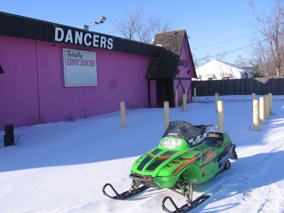 Green Arctic Cat snowmobile in snow in front of a pink building with DANCERS sign