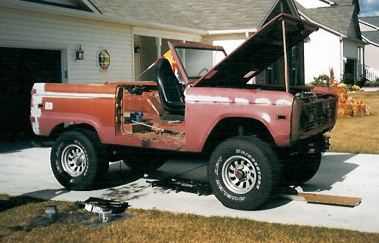 Red early Ford Bronco with doors and top removed, mid-restoration, parked in a driveway