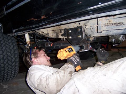 1991 Ford Bronco - A man works on the undercarriage of a black vehicle, using a power tool on the frame.