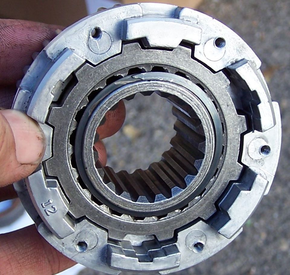 Close-up of a metal gear part with splines and teeth, held by fingers. 'J2' is visible on the outer edge