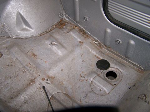 1988 Suzuki Samurai - The interior floor of the vehicle shows signs of wear and some rust, with a rubber plug near an opening.