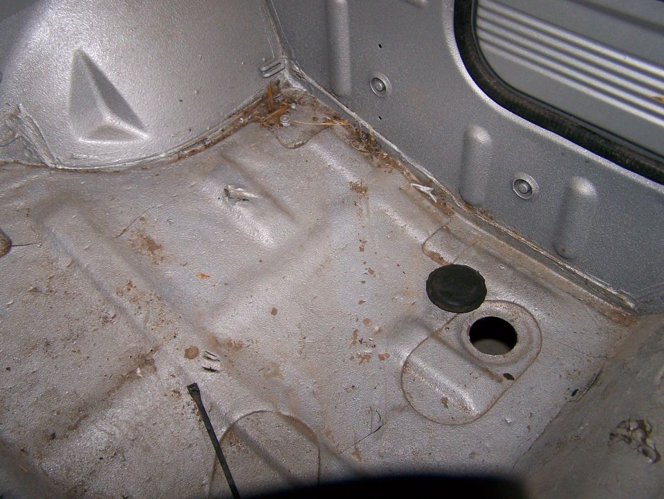 Bare silver floor pan of stripped 4x4 with rubber drain plug beside its hole