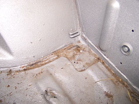 1988 Suzuki Samurai - Close-up view of the interior floor corner of a vehicle, showing dirt and rust accumulation.
