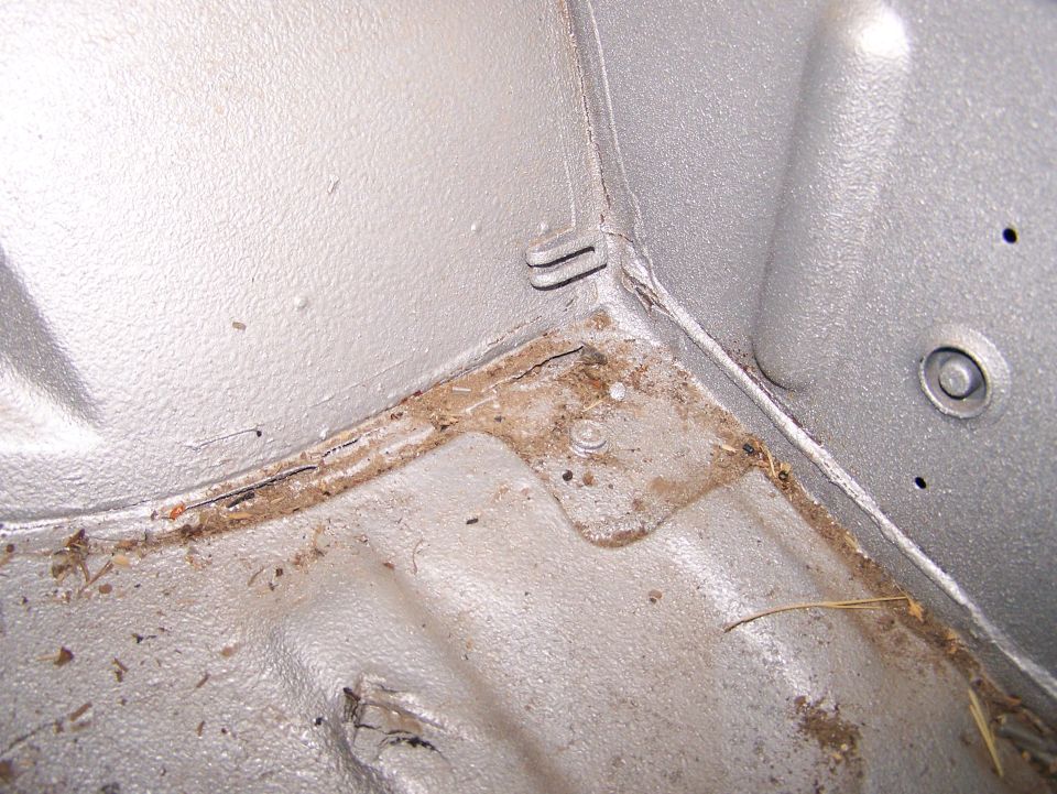 Close-up of bare silver floor pan seam with dirt, debris and light surface rust