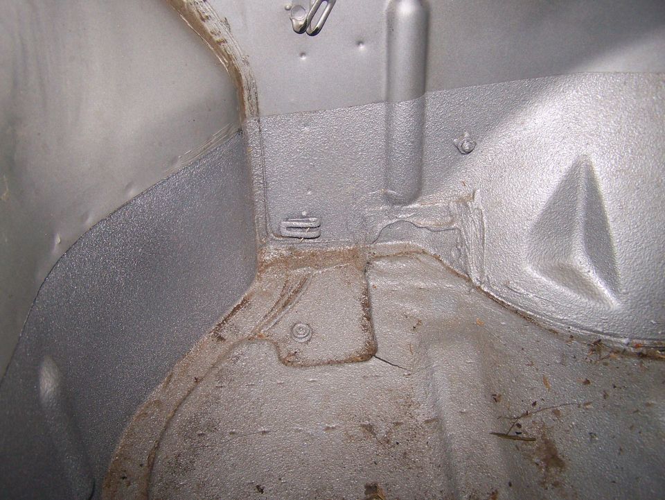 Close-up of bare gray-painted floor pan and wheel tub inside a stripped 4x4 body