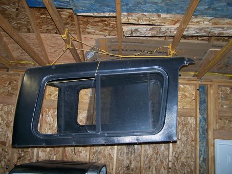 1988 Suzuki Samurai - A Suzuki Samurai hardtop is suspended from the ceiling of a garage, with another vehicle's roof visible underneath.