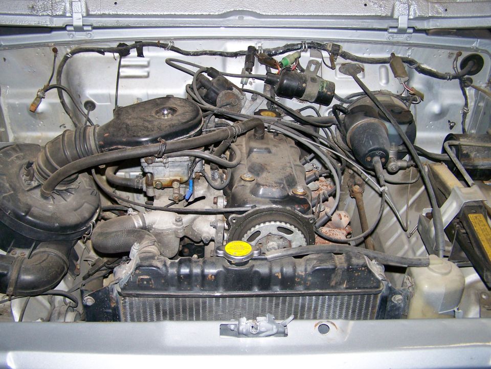 Engine bay of small four-cylinder 4x4: black air cleaner, carburetor, radiator with yellow cap