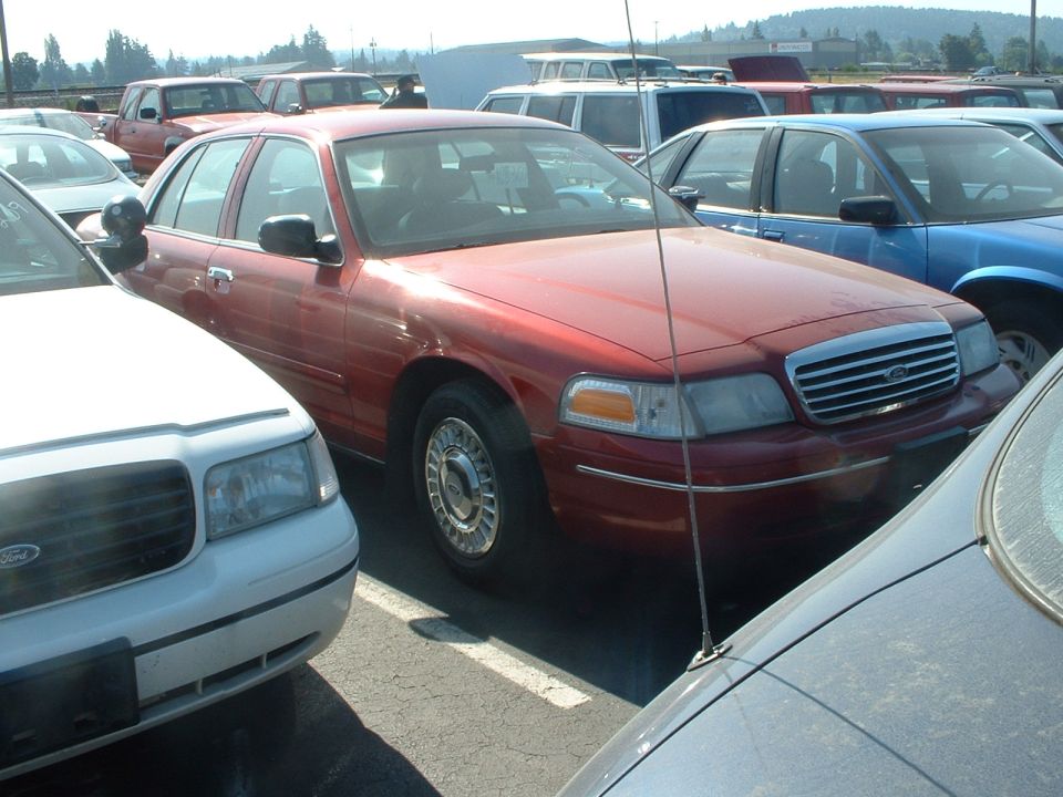 Red Ford Crown Victoria sedan parked in a busy lot, front three-quarter view
