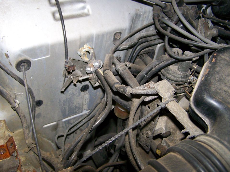 Engine bay with tangled wires, battery terminal, and hoses. Some dust is visible