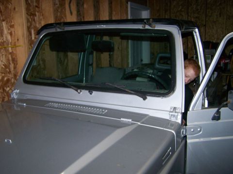 1988 Suzuki Samurai - A person is seen inside a silver Suzuki Samurai with a black soft top, parked indoors.