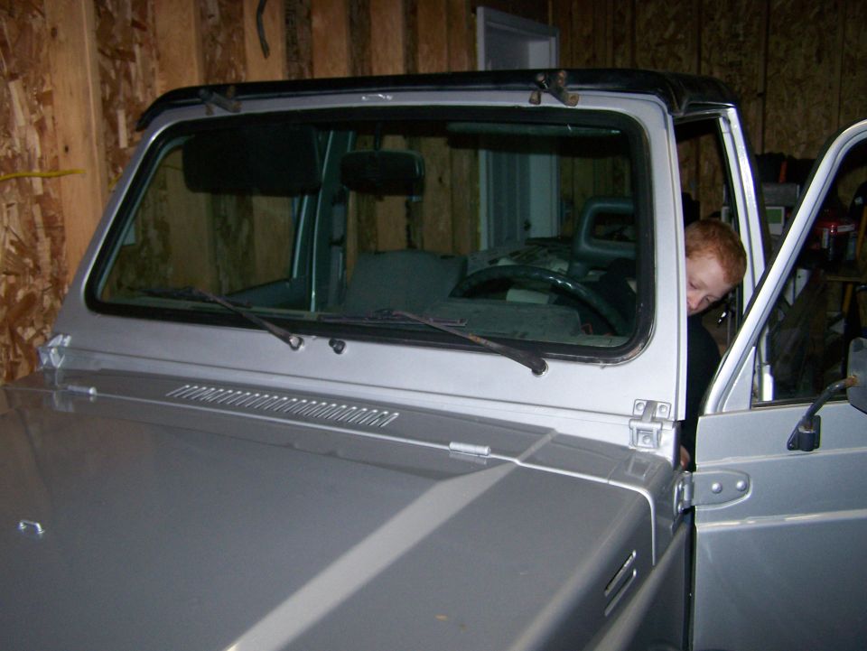 Silver Suzuki Samurai windshield frame and hood in a garage with stripped interior