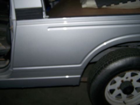 1988 Suzuki Samurai - Side view of a silver 1988 Suzuki Samurai, showing the rear wheel and body panel details.