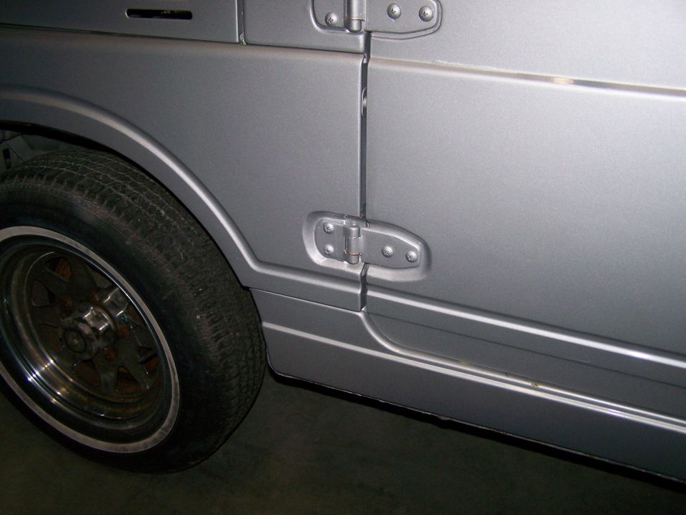 Side view of a silver SUV's door and fender with a chrome trim piece and a five-spoke wheel