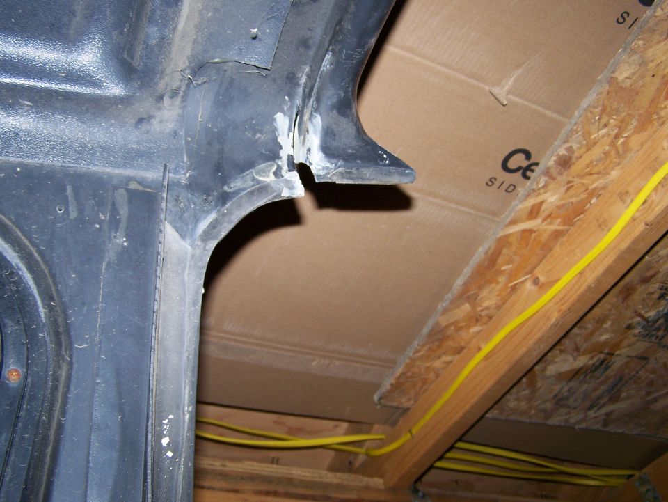 Black plastic interior of a vehicle wheel well with visible sealant and exposed wood framing above