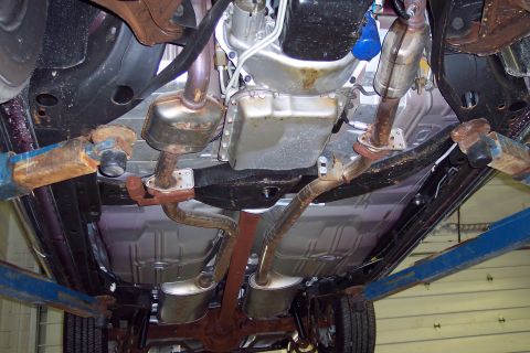 2001 Ford Crown Victoria - The undercarriage of a vehicle is shown, with focus on the exhaust pipes, mufflers, and transmission.