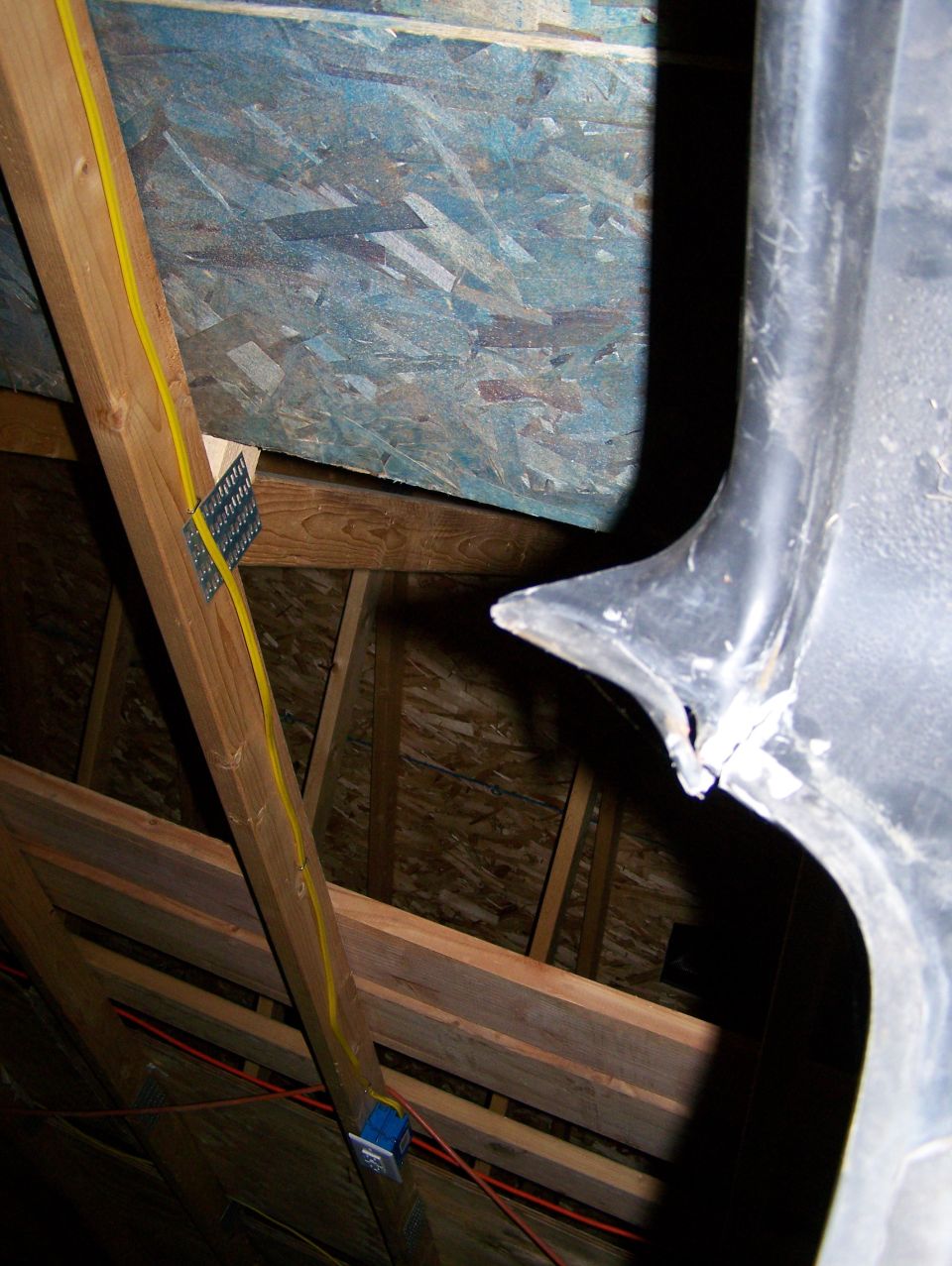 Black plastic trim piece with damage on the edge, seen in an attic with exposed wooden beams and OSB