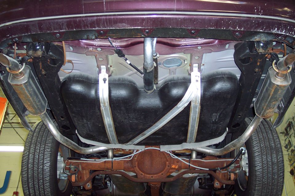 Underside of a dark purple car showing dual exhaust, fuel tank, and rear differential