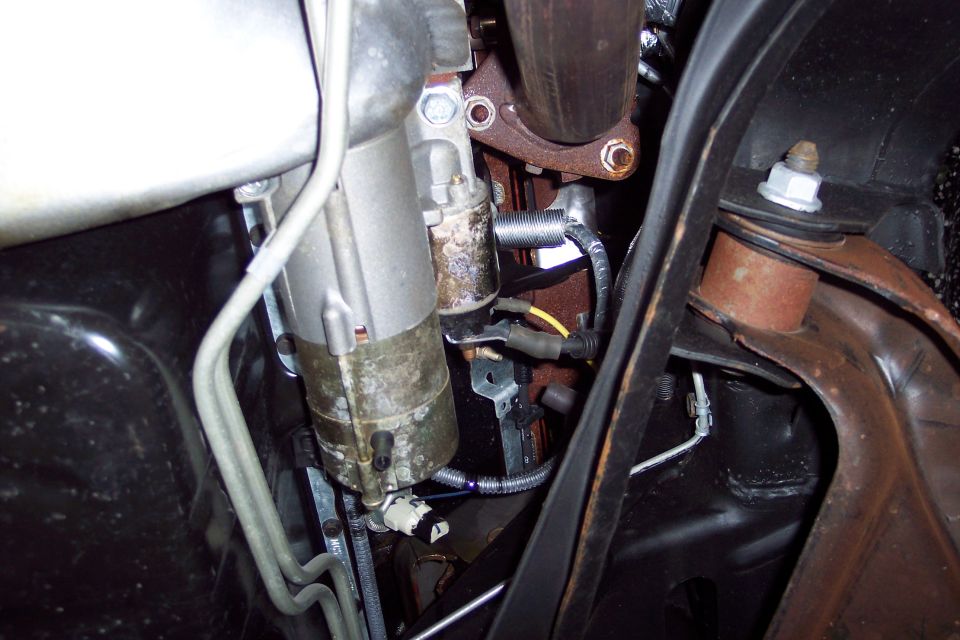 Close-up of a vehicle's starter motor and exhaust manifold, with some fuel lines visible