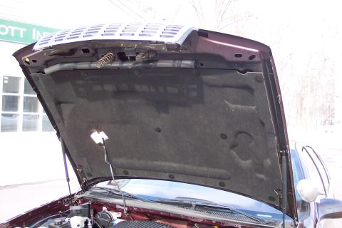 2001 Ford Crown Victoria - The engine bay of a maroon car is visible with the hood open, revealing the insulation and various engine parts.