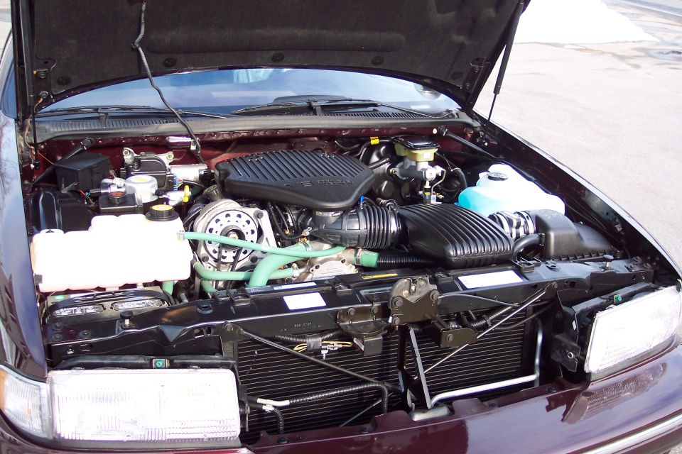 Engine bay of a maroon car with hood open. Shows engine components, hoses, and radiator
