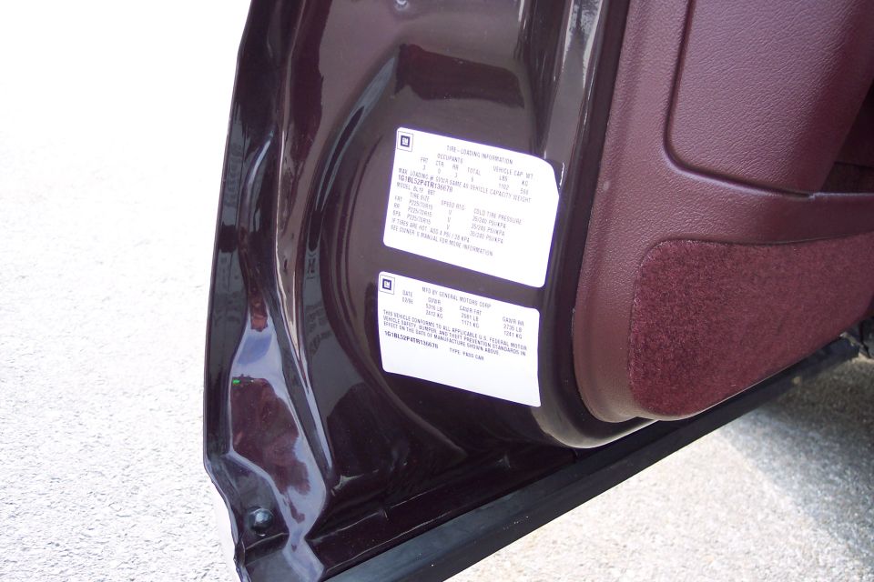 GM tire loading information label and manufacturer certification label on a maroon door edge