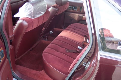 2001 Ford Crown Victoria - The interior of a maroon sedan features plush velour seats and carpeting, with a reflection visible in the rear window.