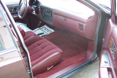 2001 Ford Crown Victoria - The interior of a car features maroon velour seats and carpeting, with a newspaper on the floor.