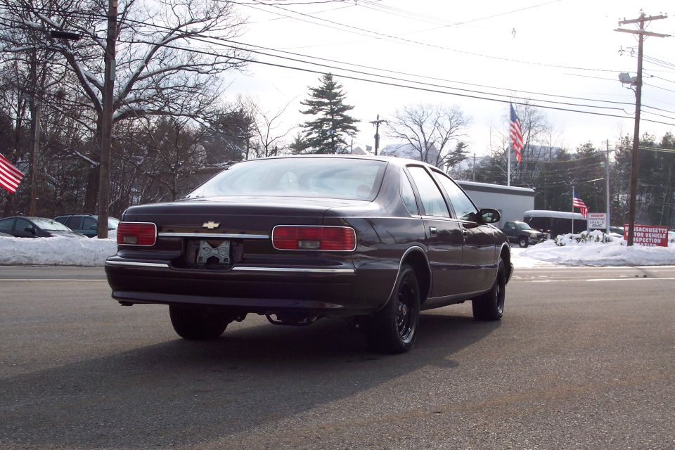 Dark sedan parked on asphalt, rear view. Snow on ground and trees