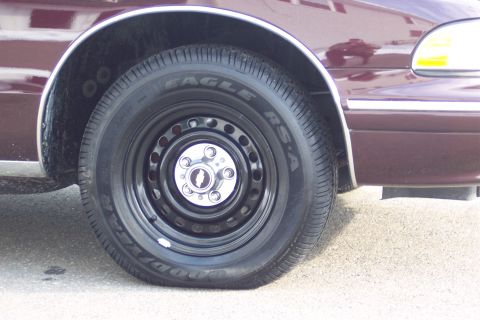 2001 Ford Crown Victoria - Close-up of a car's wheel and fender, showing a black steel wheel with a chrome center cap.