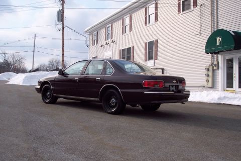 2001 Ford Crown Victoria - This maroon 1996 Chevrolet Caprice sedan is seen from the rear 3/4 angle with black wheels and snow in the background.