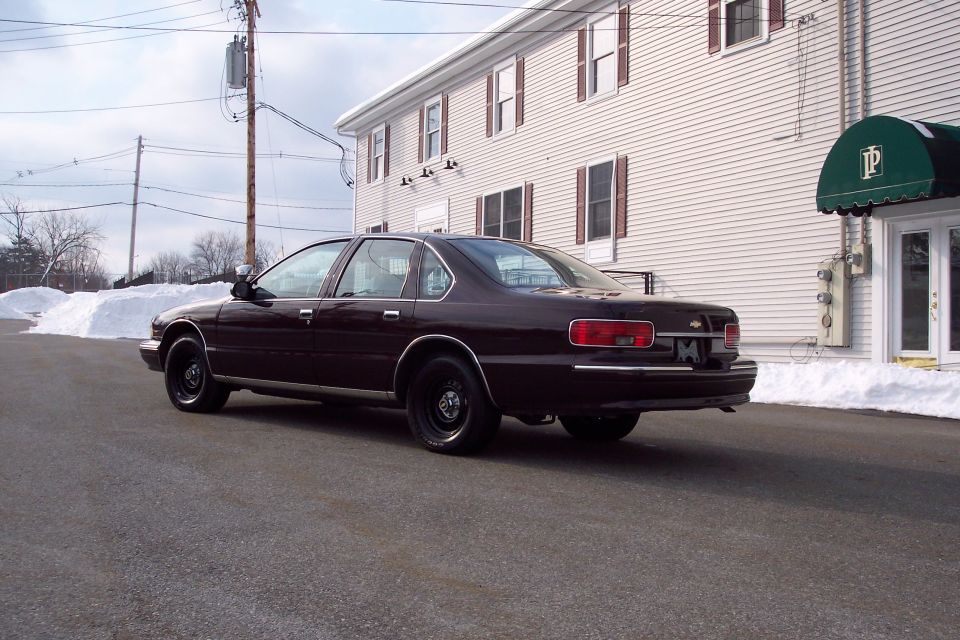 Maroon 1996 Chevrolet Caprice sedan parked on asphalt, rear 3/4 view, black wheels, snow piles in background