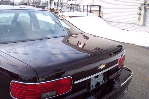 2001 Ford Crown Victoria - Rear view of a dark sedan with a Chevrolet emblem, parked near snow-covered ground.