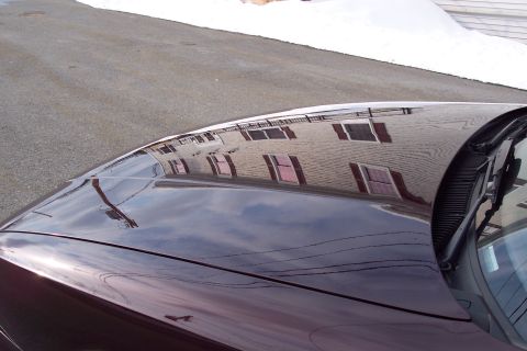 2001 Ford Crown Victoria - Reflection on the hood of a dark car shows a building with red shutters and the sky above.