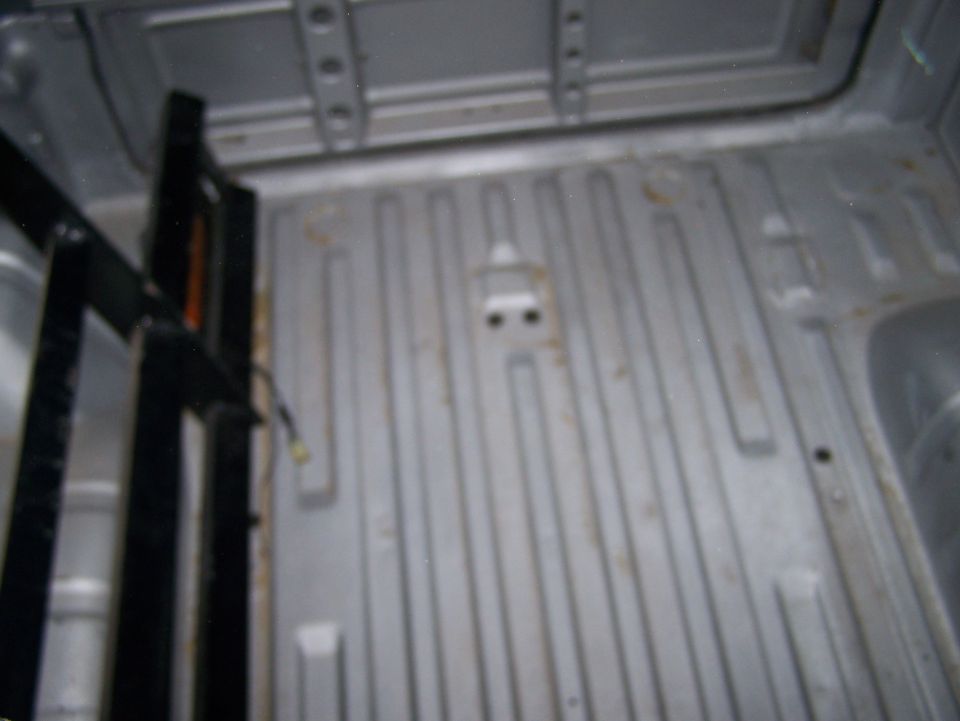 Interior of a truck bed with ribbed flooring and some black metal framing on the left