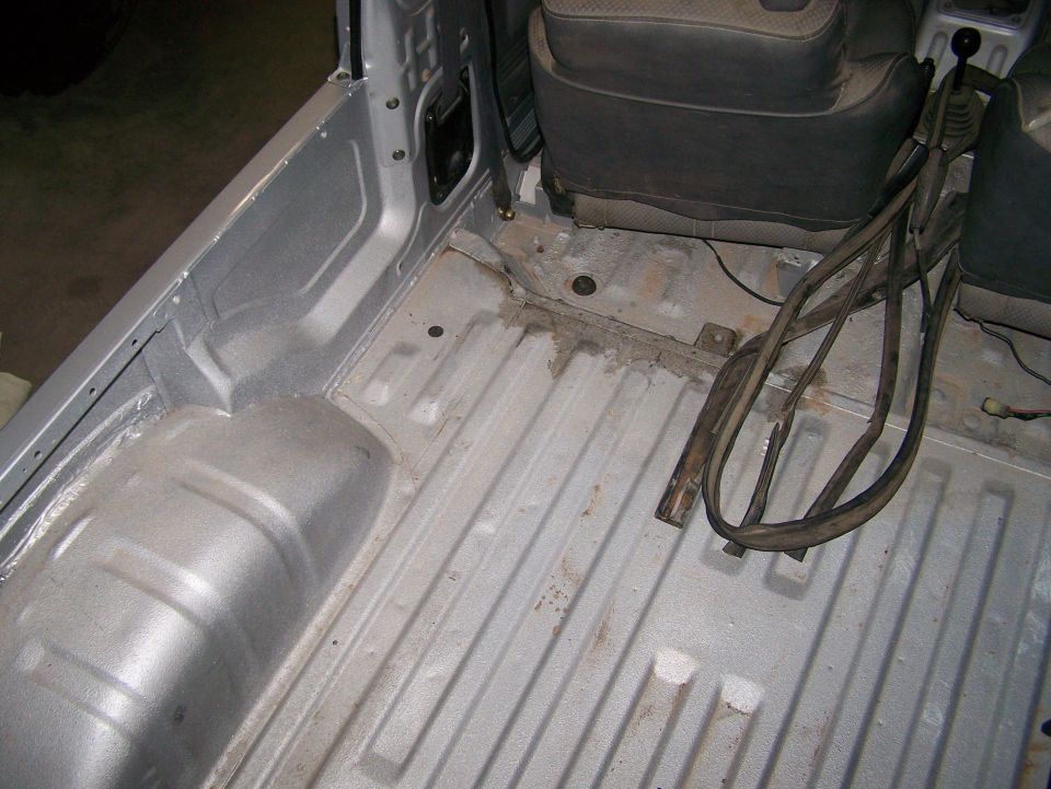 Silver vehicle bed with ribbed floor and wheel well, showing dark seats and a gear shift