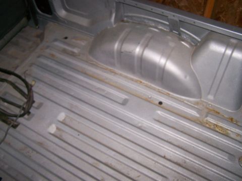 1988 Suzuki Samurai - The interior of a vehicle bed shows a ribbed floor and wheel well with signs of rust.
