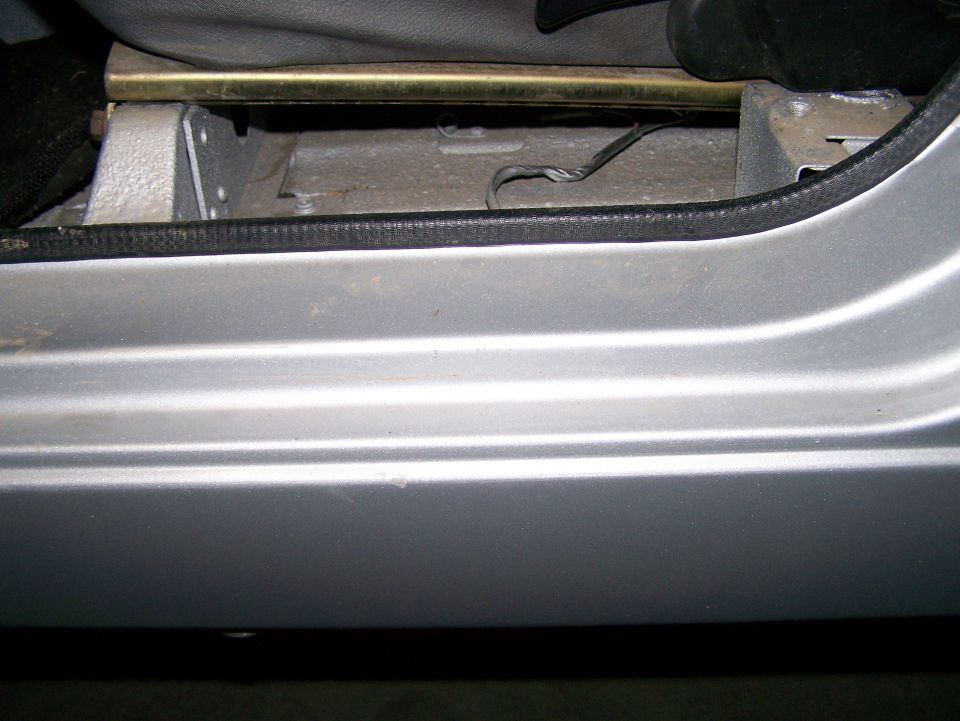 Silver vehicle door sill with visible seat mounting hardware and wiring