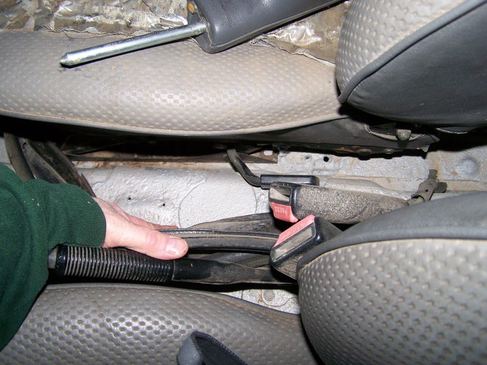 Hand operating parking brake lever between vehicle seats, showing seatbelt buckles